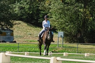Amazona conduz um cavalo em uma arena externa de adestramento cercada por vegetação.