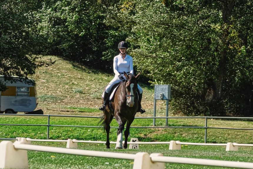 Amazona conduz um cavalo em uma arena externa de adestramento cercada por vegetação.